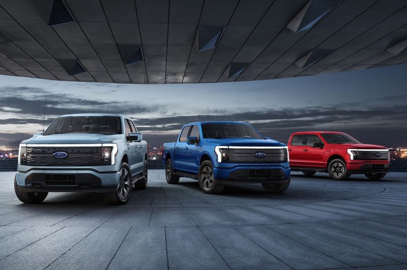 Three Ford F-150 Lightning models parked with red, blue and gray colors.