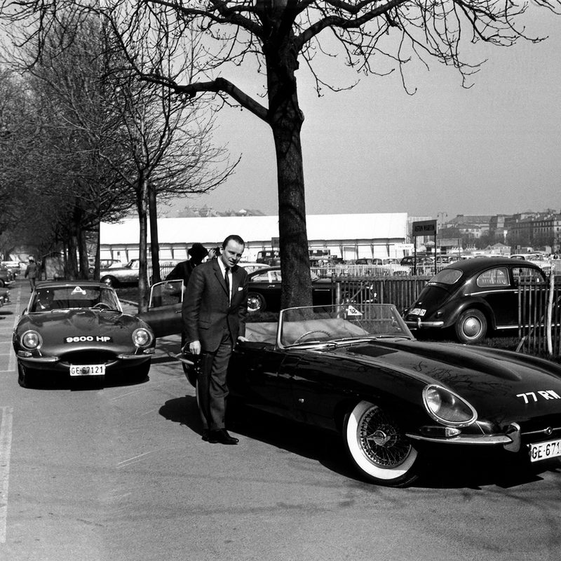 An old photo of a man standing next to a Jaguar e-type