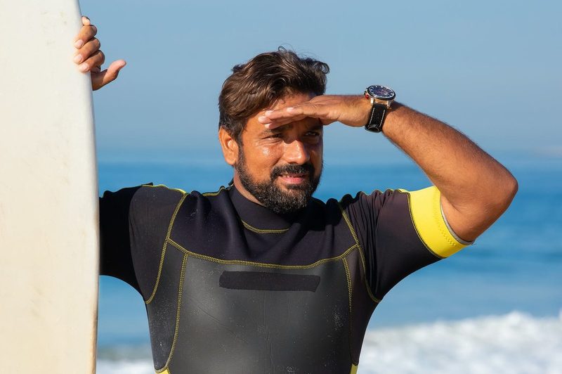 Man shielding eyes from the sun next to surfboard