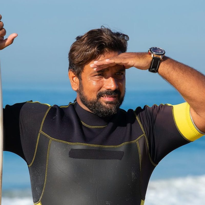 Man shielding eyes from the sun next to surfboard