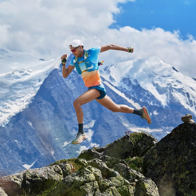 A Hoka Athlete runs across an Alpine ridge with mountains in the background.