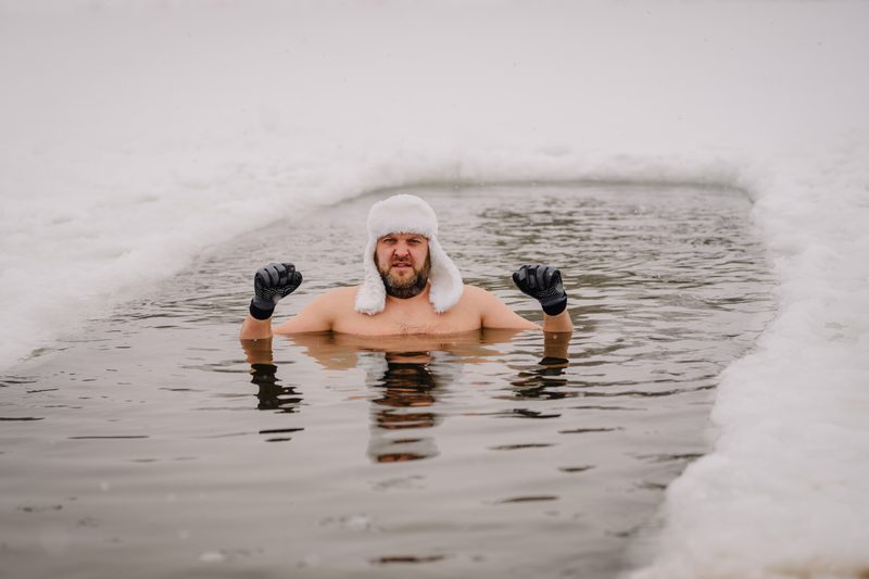 Man wearing a white hat and black gloves swimming in a hole in the ice