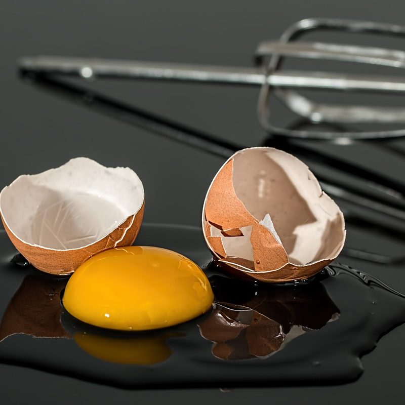 Broken egg with an egg beater on a black surface