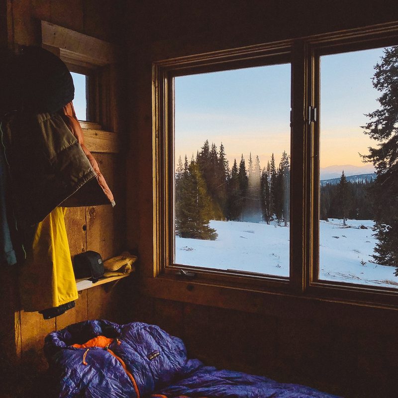 A sleeping bag inside a camping hut with snow on the ground outside.