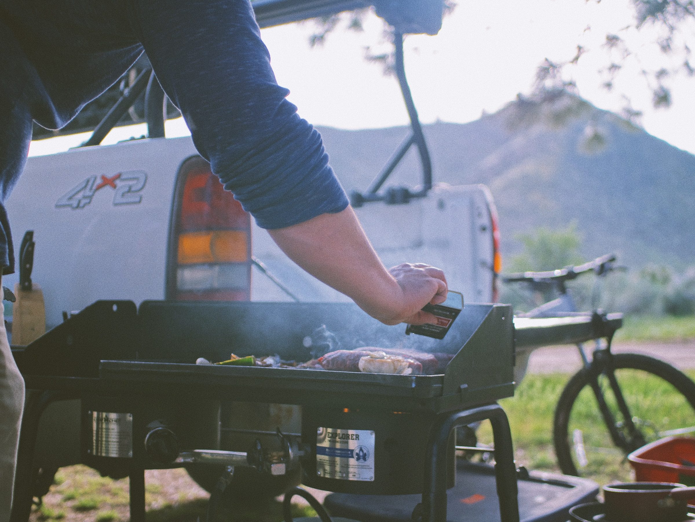 A man grills in a campsite with a truck behind him.