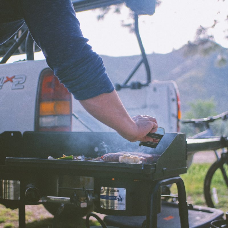 A man grills in a campsite with a truck behind him.
