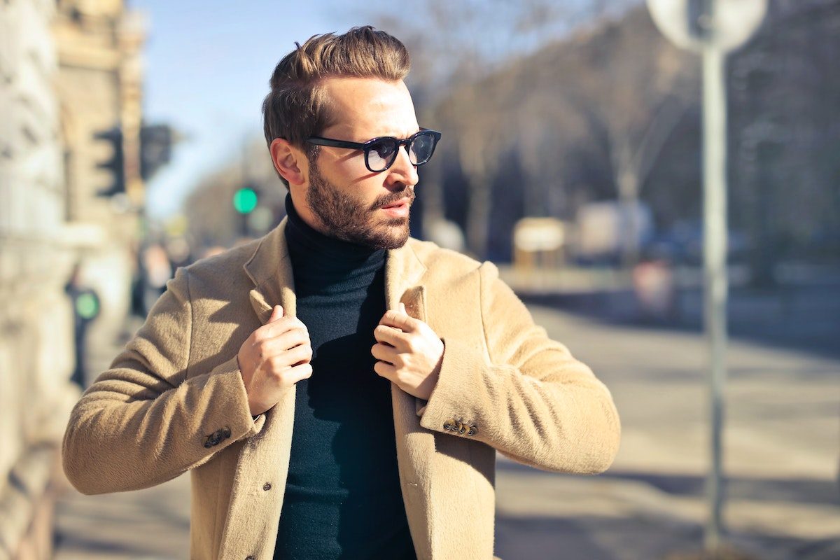 a man with a beard and light jacket walking down a street