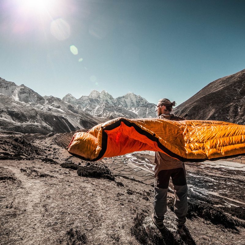 A man stands on the mountain with a sleeping bag around him.