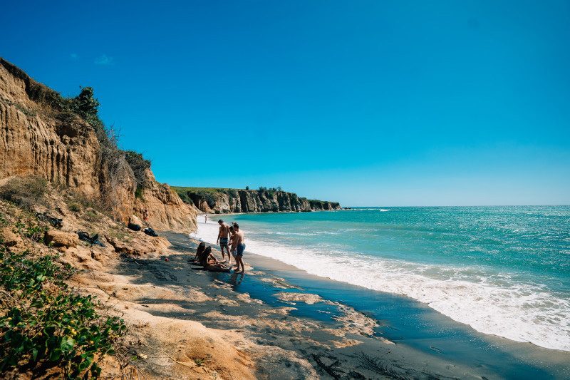 Group of people enjoying the sun and waves at Puerto Rico's Playa Negra black sand beach.