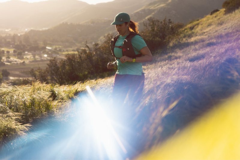 Woman trail running down a hill with houses in the background.