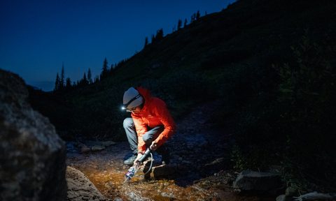 A man collects water from a river by the light of a headlamp.