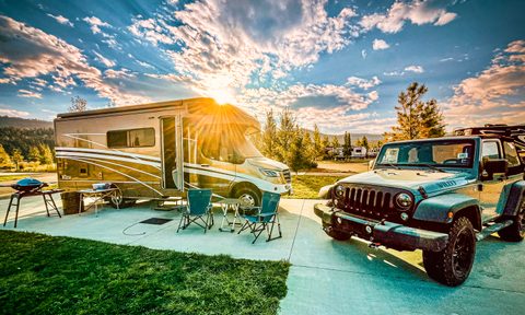 An RV and a Jeep at a campground with the setting sun in the background.