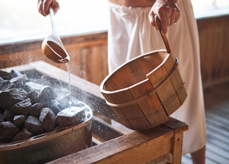 A man sprinkling water on sauna rocks with a bucket and ladle