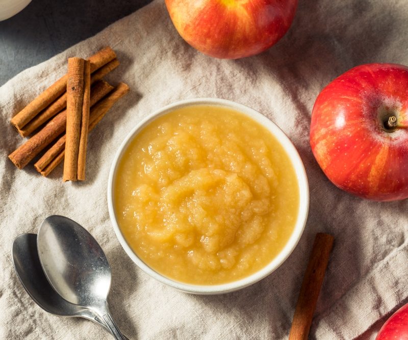 Applesauce in a bowl surrounded by cinnamon and apples.