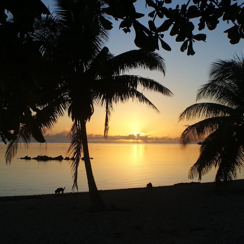 Sunset over a dark sandy beach in Tahiti.