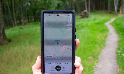 A person walks in the woods with their phone open and AllTrails running.