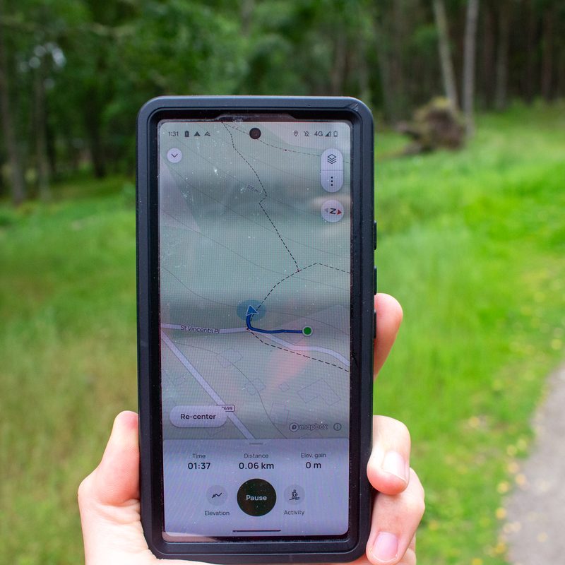 A person walks in the woods with their phone open and AllTrails running.