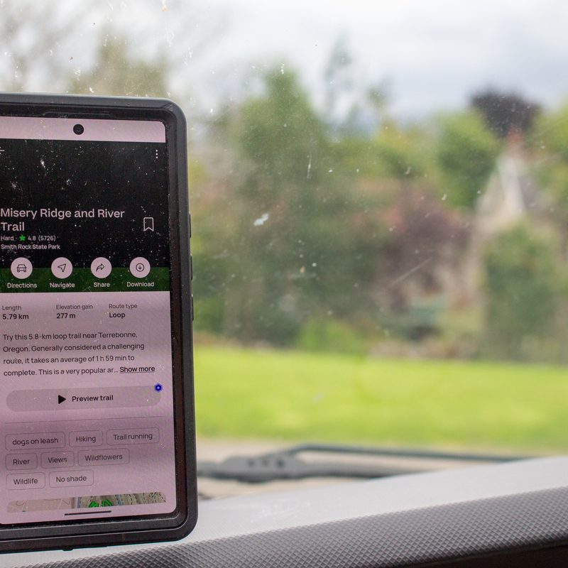 A phone with All Trails on the dashboard of a vehicle.