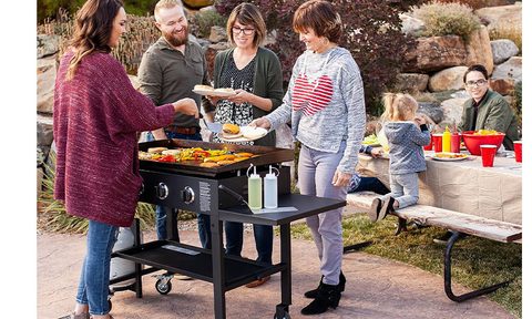THe Blackstone 36-inch Gas Griddle Cooking Station in a yard with people around it cooking and enjoying themselves.