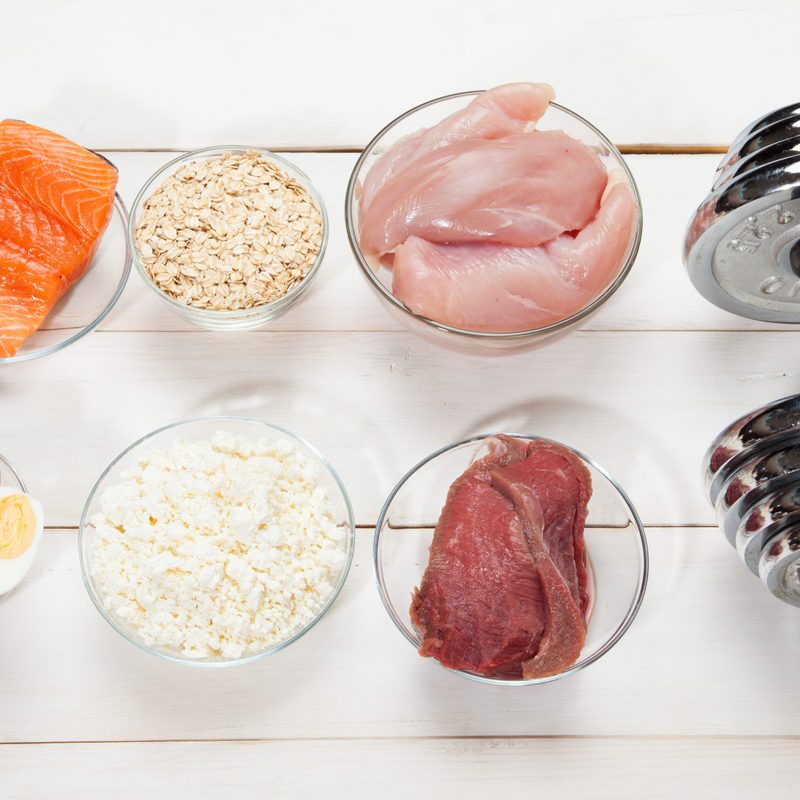 Protein food sources on a surface next to a bar bell