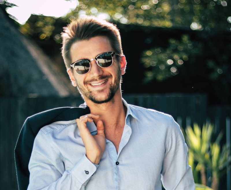 Man in round sunglasses with jacket on his shoulder