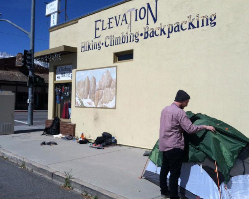 Man pitching a tent right outside Elevation outdoor gear store in Lone Pine, California.