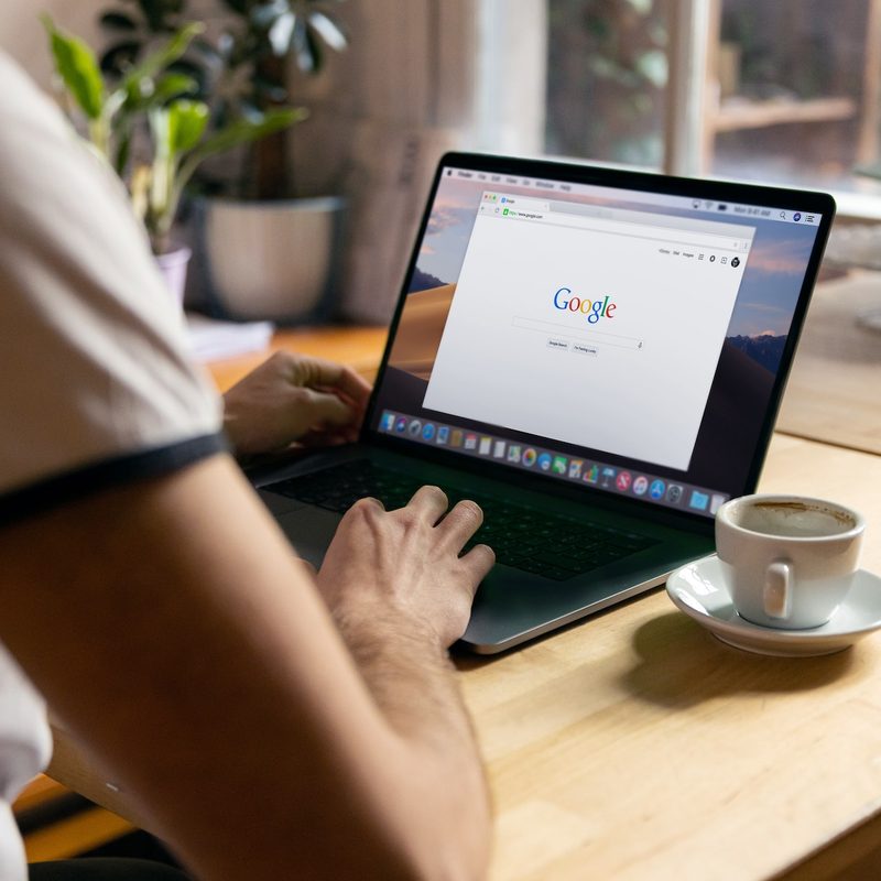 A man's shoulder and hands as he types on a laptop with a Google browser open