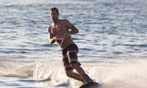 Wakeboarder in colorful shorts riding in sunset.