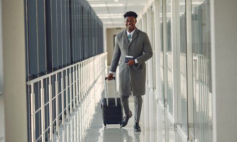 Well-dressed man rolling a luxury carry-on bag through a private plane terminal hallway