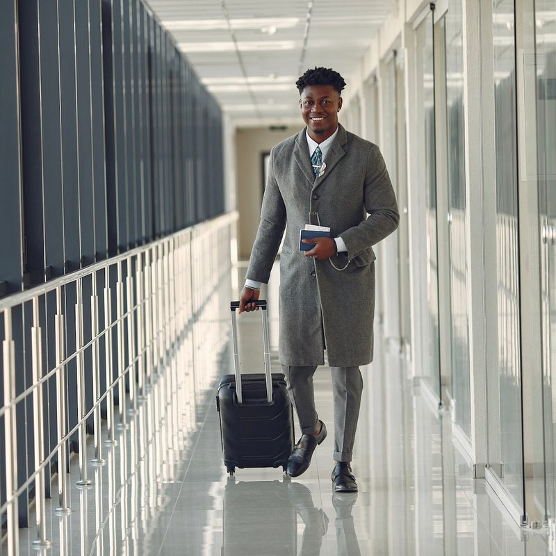 Well-dressed man rolling a luxury carry-on bag through a private plane terminal hallway