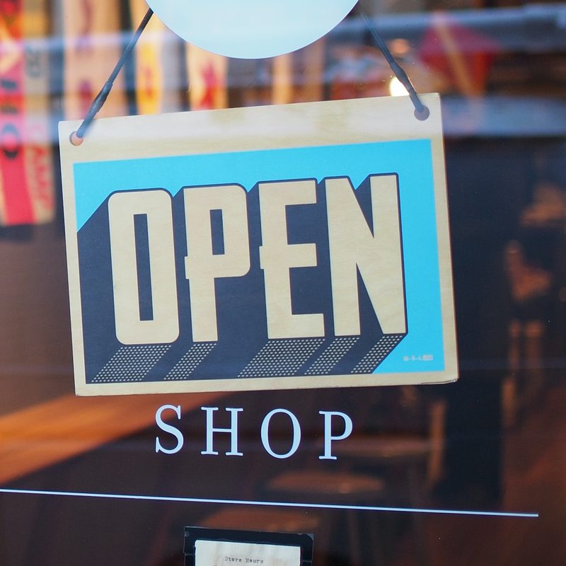 Gray and blue "OPEN" sign hanging on a the front door of a small shop.