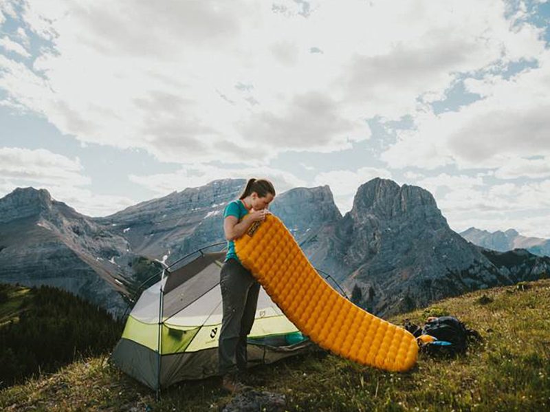Young woman standing on a hill inflating a Nemo Tensor sleeping pad.