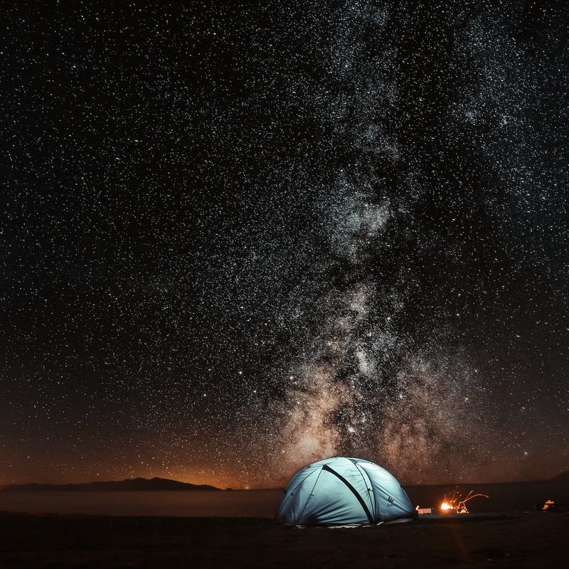 A single tent lit from the inside under a clear night sky with views of the Milky Way.