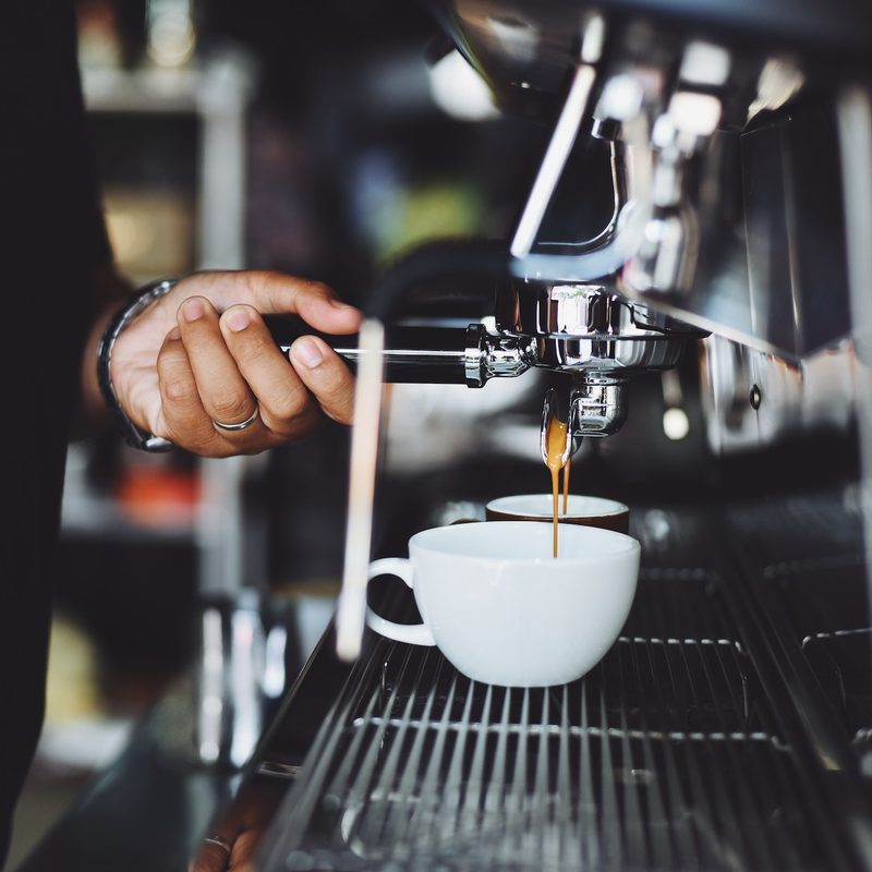 A person making coffee at an industrial coffee machine.