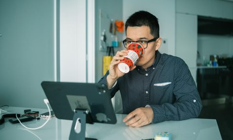 A person sitting at their work desk drinking out of a Starbucks cup.