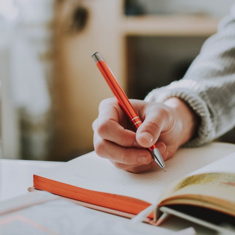 a person with a gray sweater writing with a pen