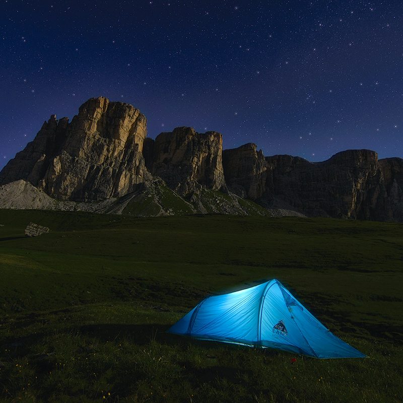 Lone blue tent lit from the inside in a desert landscape at night.