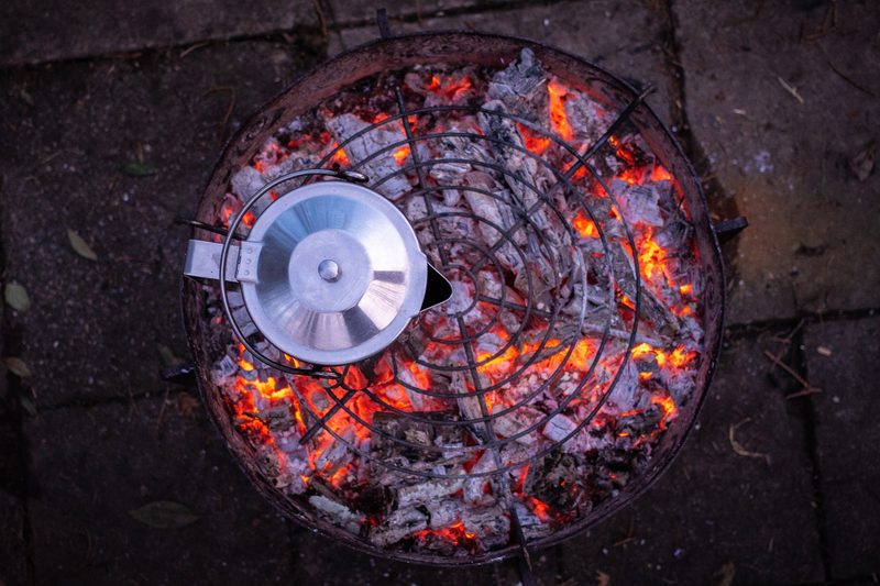 Stainless kettle heating over a campfire grate.