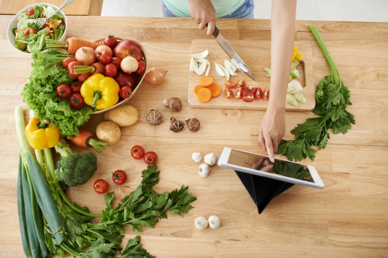 Person chopping vegetables while looking at a recipe.