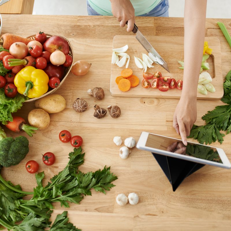 Person chopping vegetables while looking at a recipe.