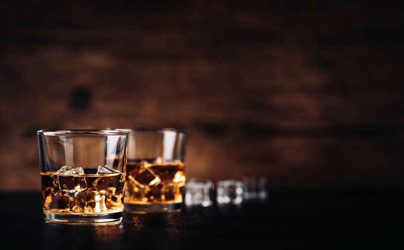 Whisky, whiskey, bourbon or cognac with ice cudes on black stone table and wood background