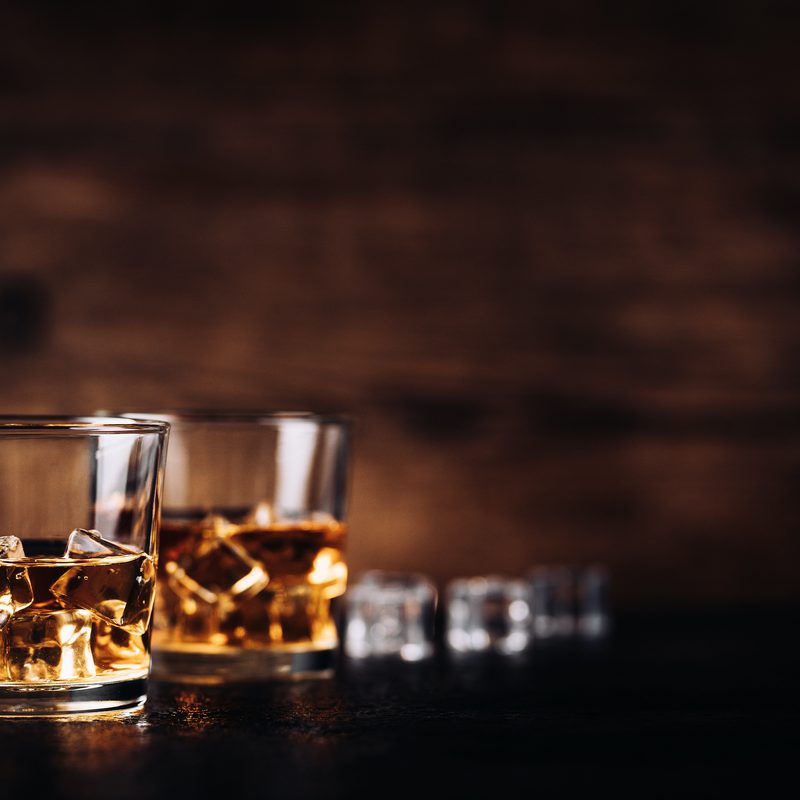 Whisky, whiskey, bourbon or cognac with ice cudes on black stone table and wood background