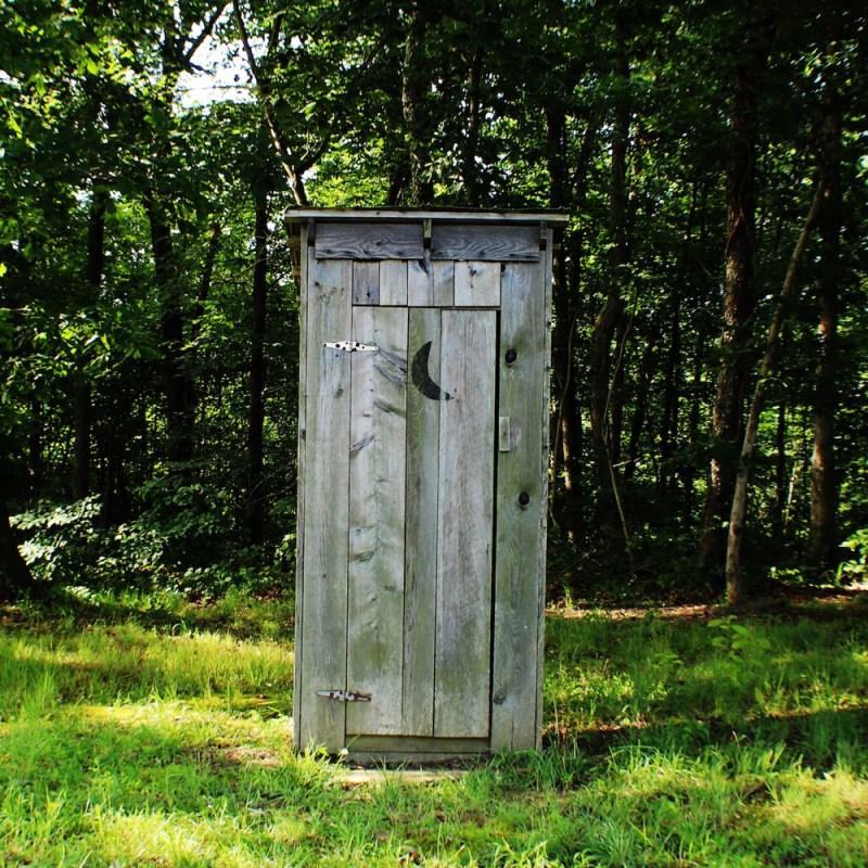 A wooden outhouse with a crescent moon cutout on the door.