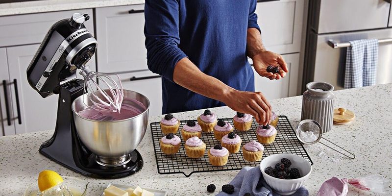 The KitchenAid Classic Series 4.5 Quart Tilt-Head Stand Mixer being used on a kitchen tabletop with food around it.