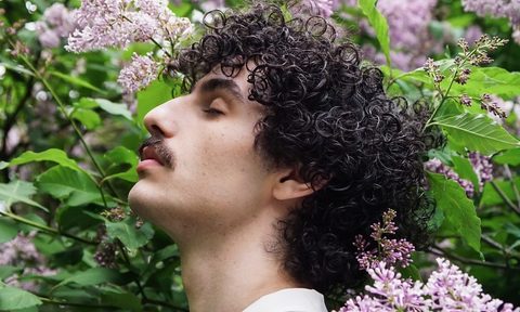 Man with brunette hair standing in front of flowers.