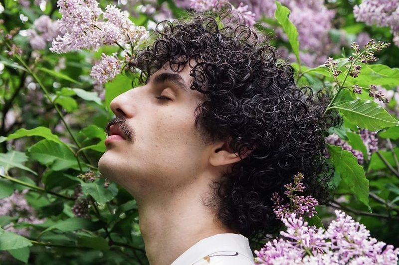 Man with brunette hair standing in front of flowers.
