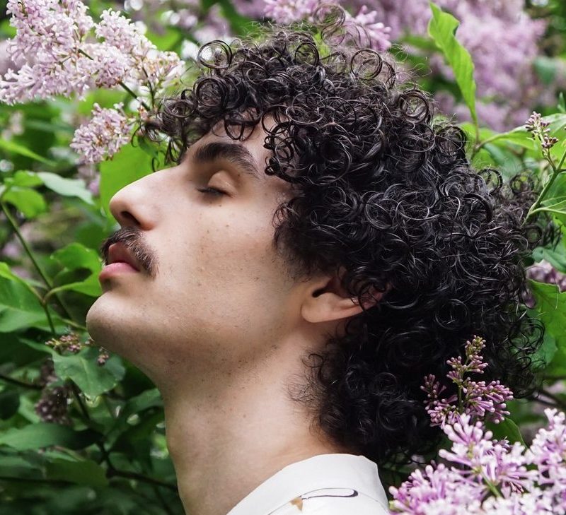 Man with brunette hair standing in front of flowers