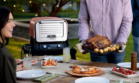 Ninja Woodfire 8-in-1 Outdoor Oven with Pizza in oven against a white background and accessories