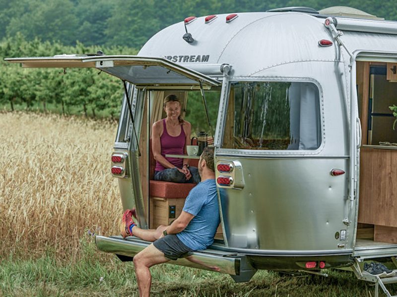Couple sitting on the rear hatch of the Airstream Trade Wind travel trailer.