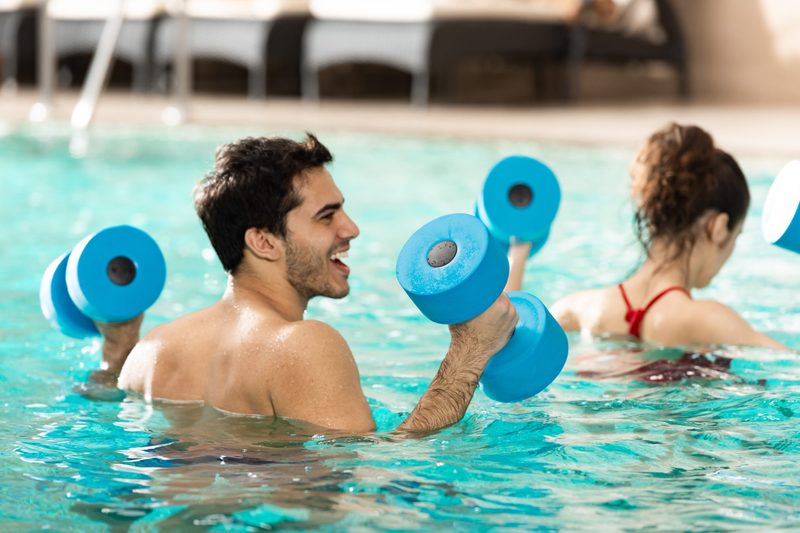 Selective focus of cheerful man with dumbbells during water aerobics in swimming pool